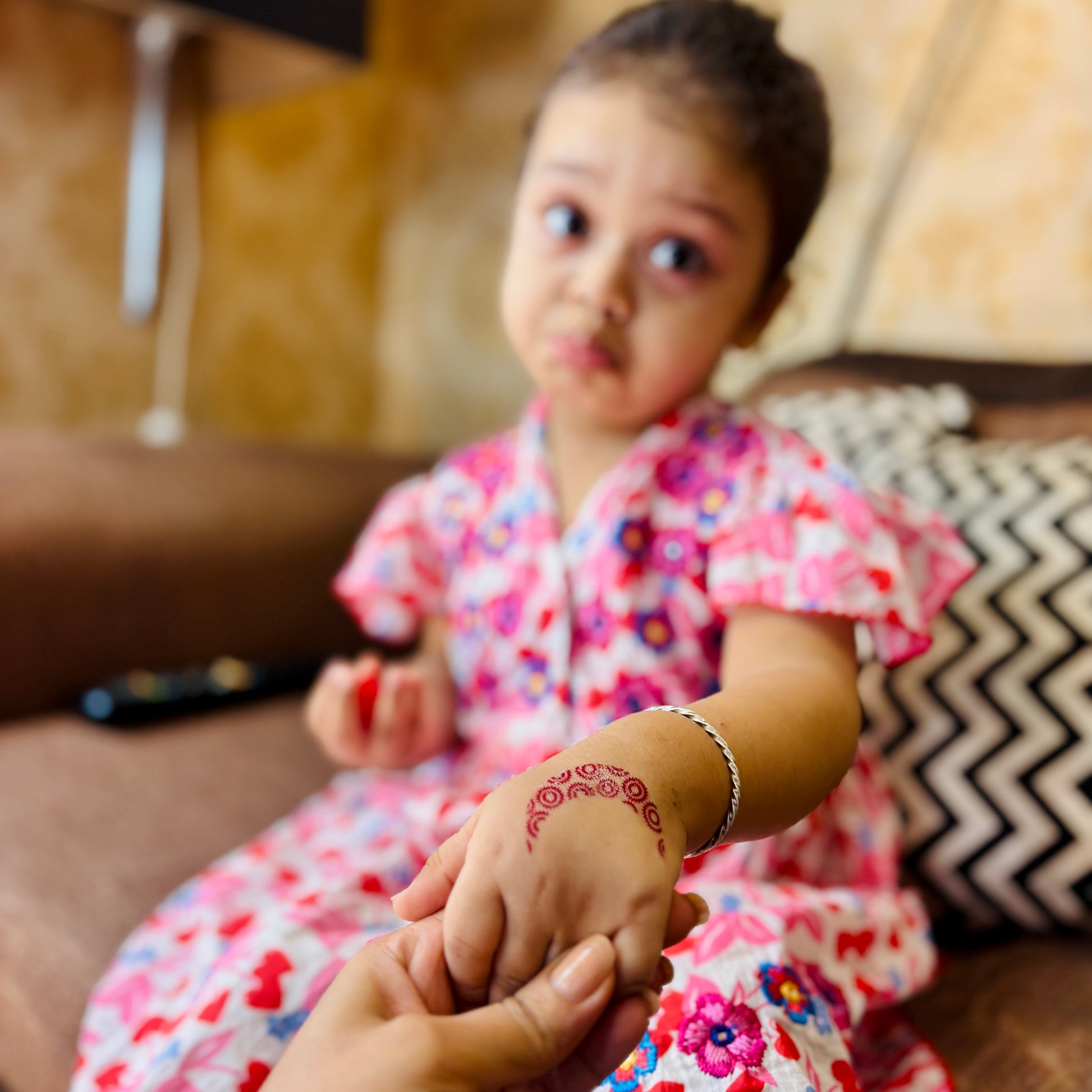 Child in a floral dress holding an adult's hand, with a blurred background