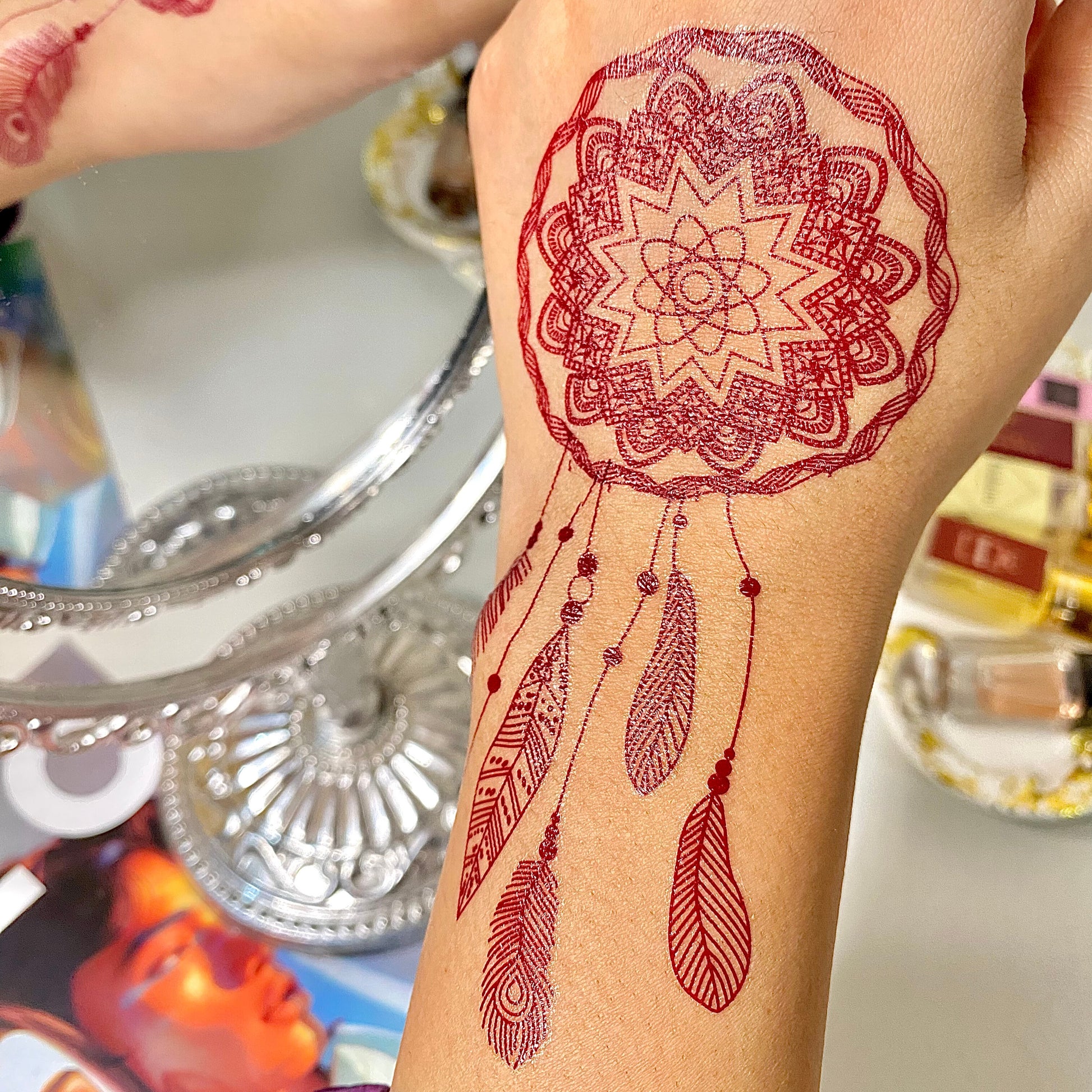 Red mandala tattoo with feathers on a person's arm, blurred background