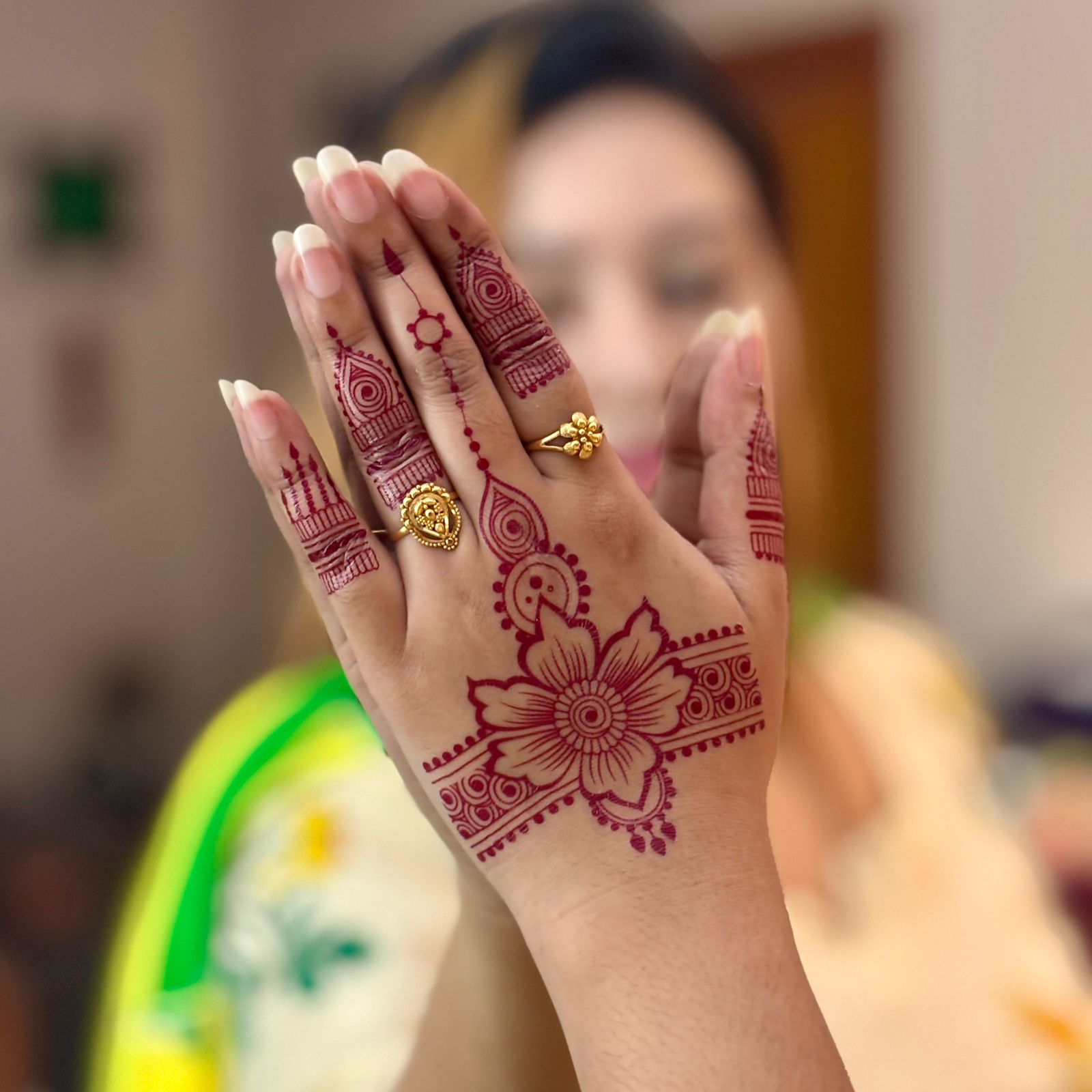 Hand with intricate henna design and a gold ring, blurred background