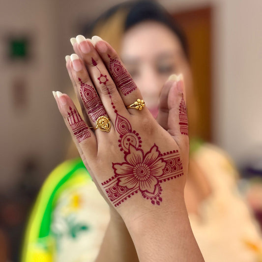 Hand with intricate henna design and a gold ring, blurred background