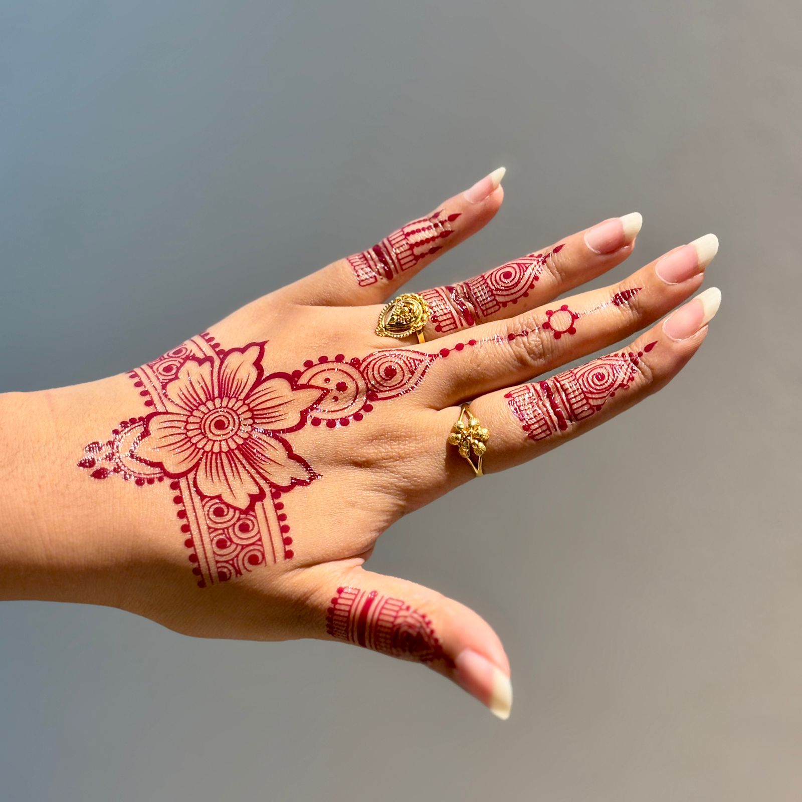 Hand with red henna designs and gold rings against a blurred background