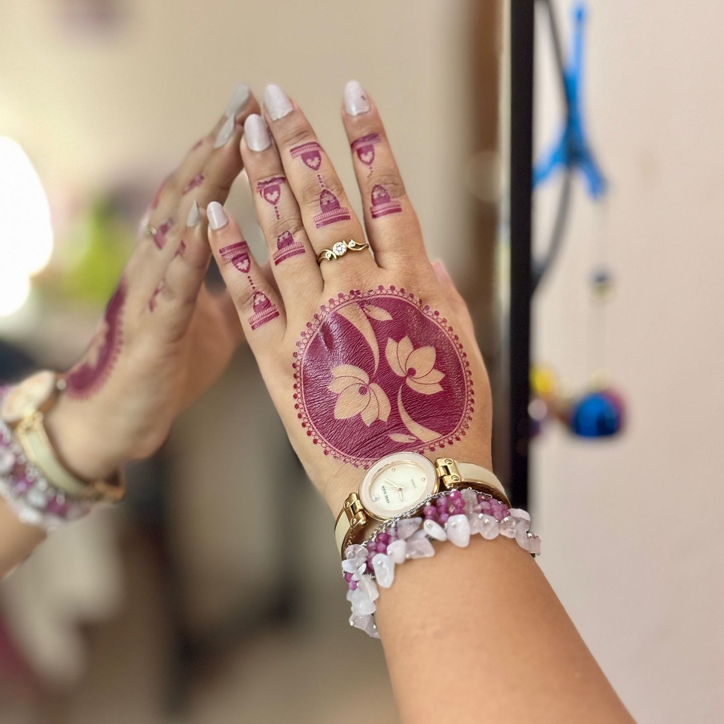 Hand with intricate henna design, gold watch, and bracelets against a blurred background