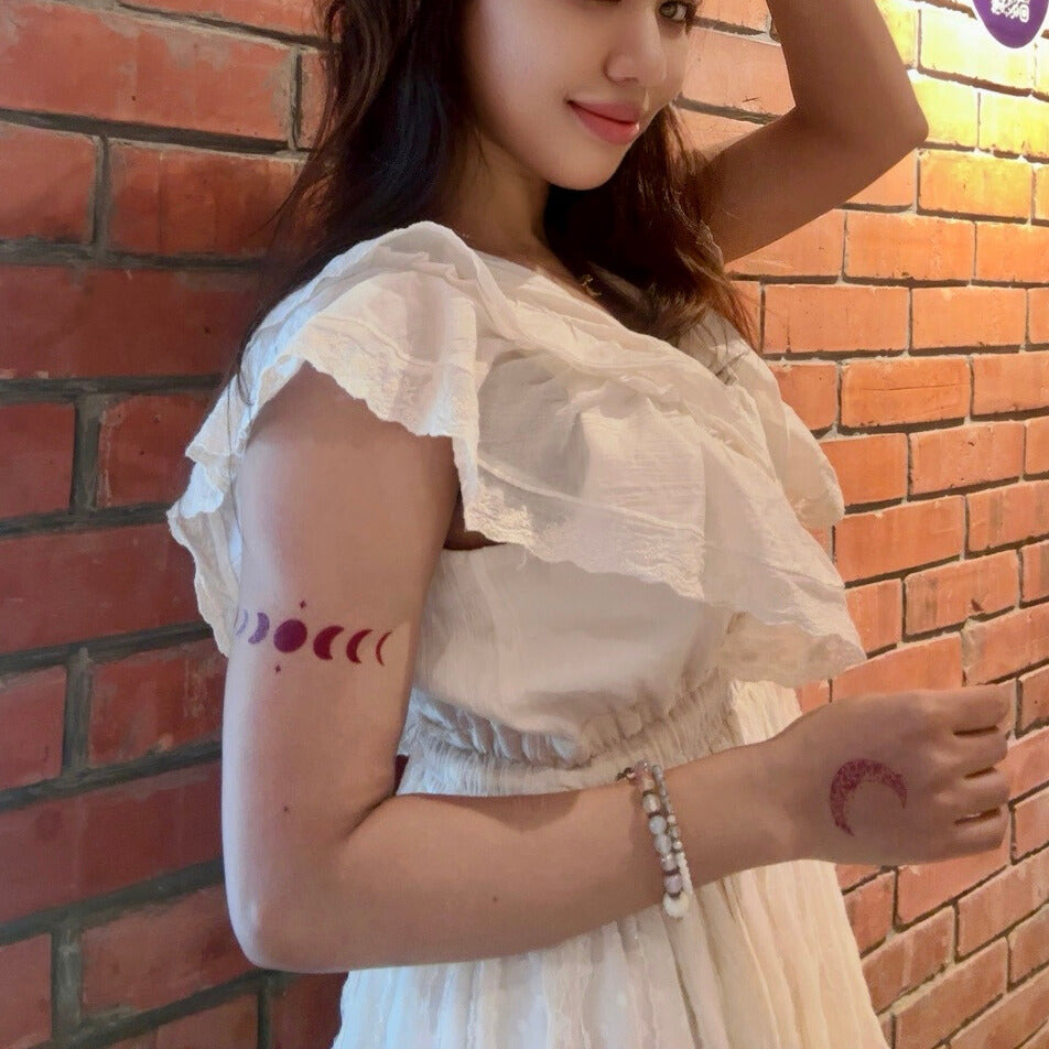 Woman with moon phase tattoos on her arms standing against a brick wall.