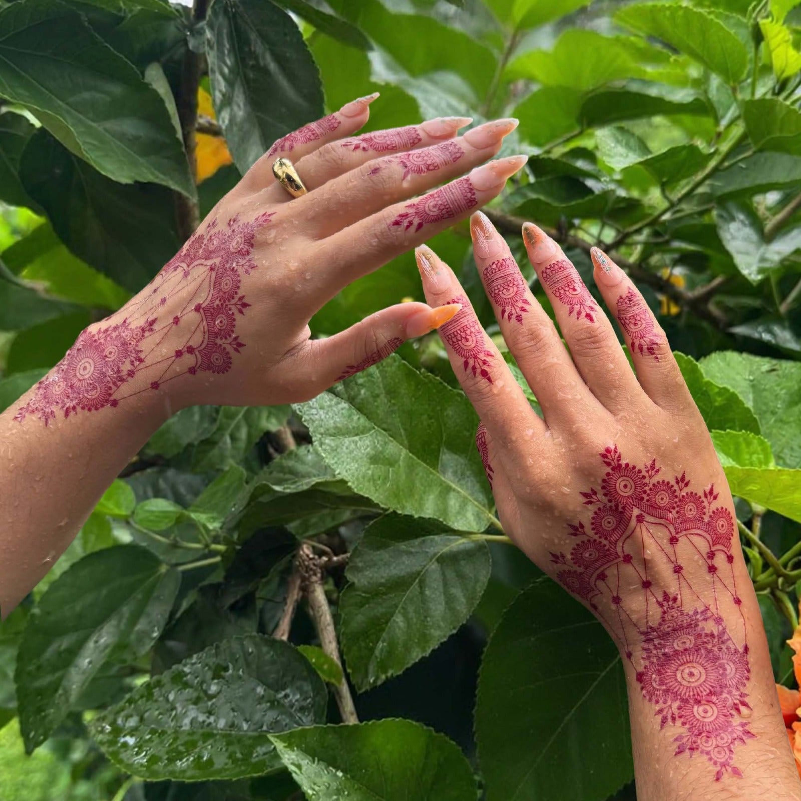 Hands with pink henna designs against a green leafy background