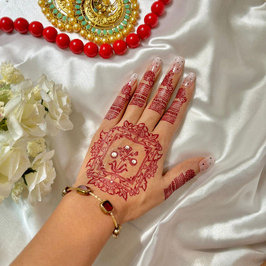 Hand with intricate red henna design on a white fabric background with red beads and flowers.