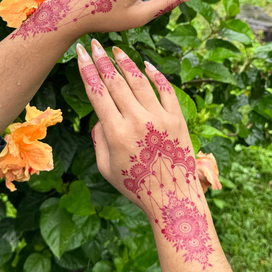 Hand with pink henna design against a green leafy background