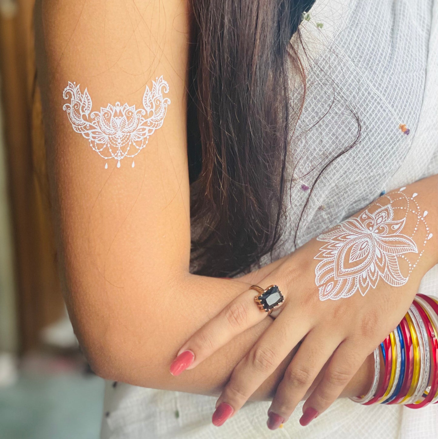 Woman with white floral temporary tattoos on her arm and hand, wearing a ring and colorful bangles.